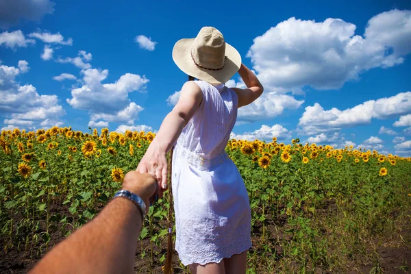 Folge mir, junge Frau hält einem Mann ein Feld mit Sonnenblumen in der Hand — Stockfoto