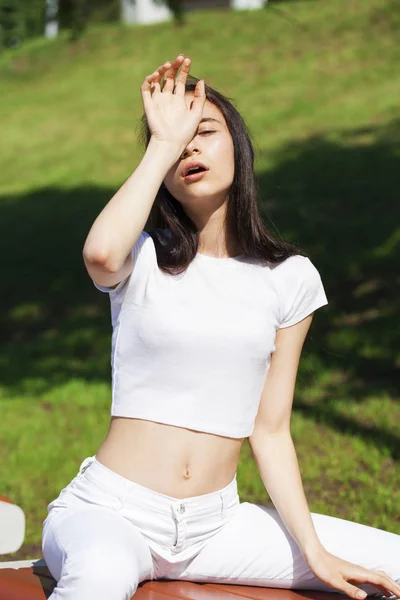 Beautiful brunette woman posing against summer park, bright sunn — Stock Photo, Image