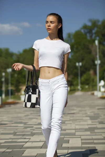 Jonge mooie brunette meisje in witte jeans en t-shirt wandelen — Stockfoto