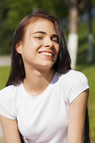 Beautiful brunette woman posing against summer park, bright sunn — Stock Photo, Image