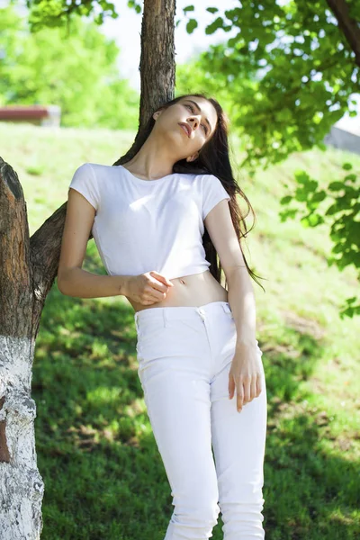 Hermosa mujer morena posando contra el parque de verano, sol brillante —  Fotos de Stock