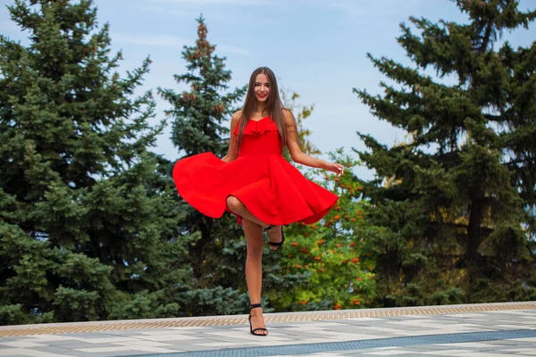 여름 거리에서 걷는 빨간 드레스를 입은 젊은 아름다운 소녀 — 스톡 사진