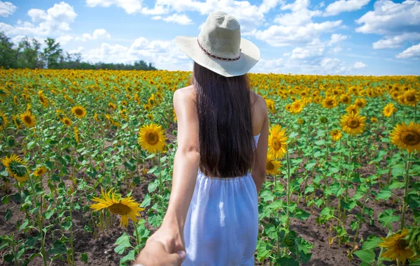 Volg mij, jonge vrouw het houden van een man hand een veld van zonnebloemen — Stockfoto