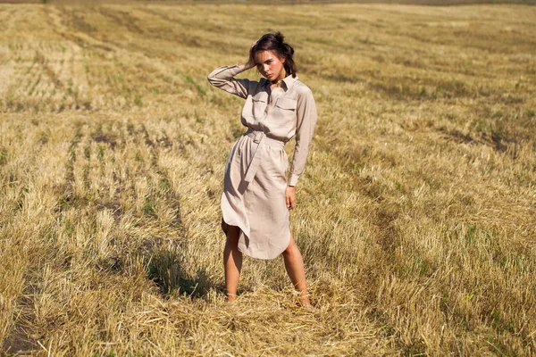 Joven modelo morena hermosa en un vestido beige posando contra t —  Fotos de Stock