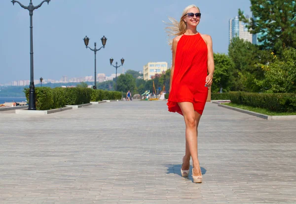 年轻的美丽的女人在红色礼服走在夏天的大街上 — 图库照片