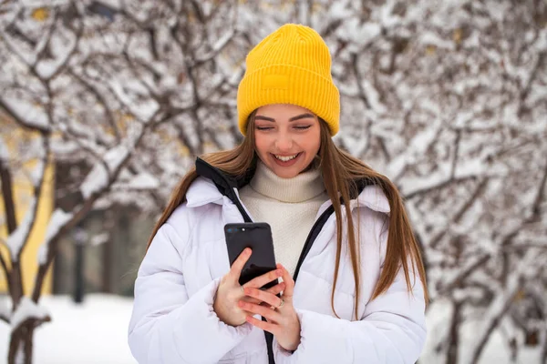 Νεαρή όμορφη γυναίκα με κινητό τηλέφωνο σε χειμερινό πάρκο — Φωτογραφία Αρχείου