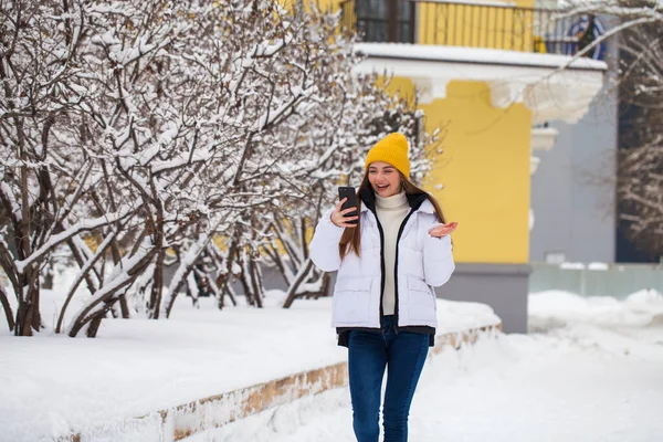 Młoda piękna kobieta z telefonem komórkowym w parku zimowym — Zdjęcie stockowe