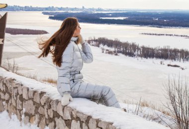 Gümüş renkli kayak takımlı, tepede poz veren esmer bir kadın.
