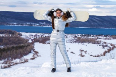 Gümüş renkli kayak takımlı, tepede poz veren esmer bir kadın.