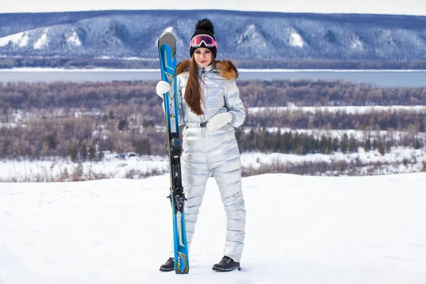 Молодая брюнетка в серебряном лыжном костюме позирует на вершине холма — стоковое фото
