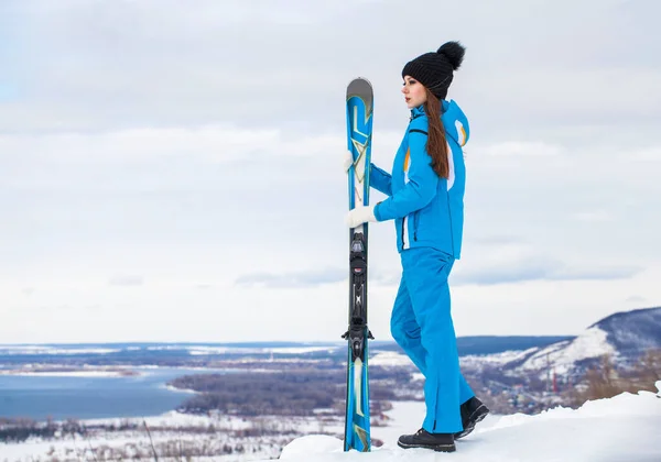 Νεαρή μελαχρινή γυναίκα με κοστούμι του σκι που ποζάρει στην κορυφή ενός λόφου — Φωτογραφία Αρχείου