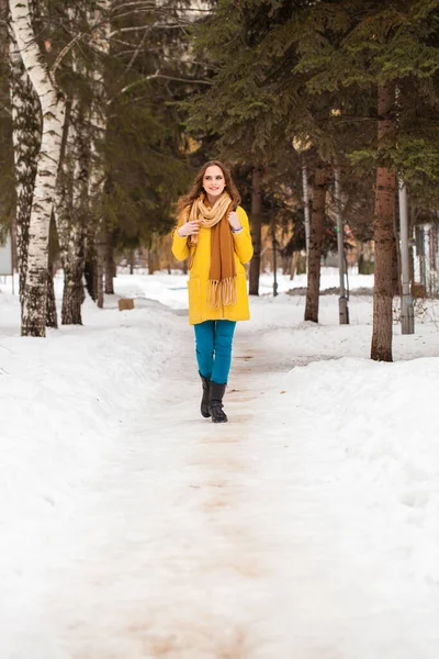 若いです美しい女性で黄色のコート歩く冬の公園 — ストック写真