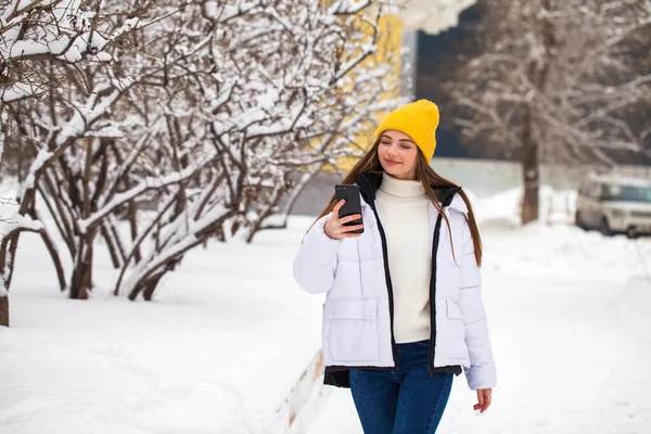 Молодая красивая женщина с мобильным телефоном в зимнем парке — стоковое фото