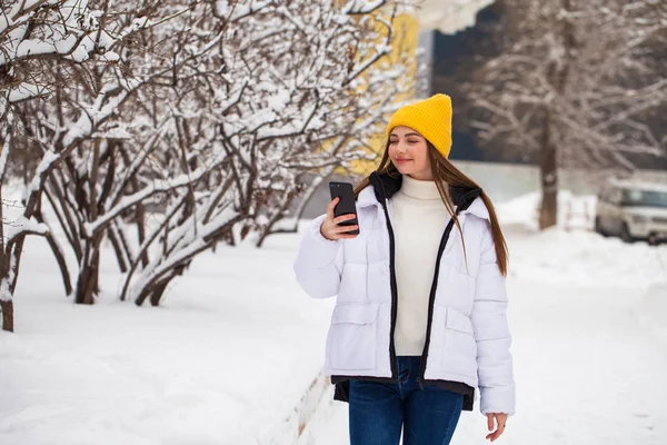 Giovane bella donna con un telefono cellulare in un parco invernale — Foto Stock