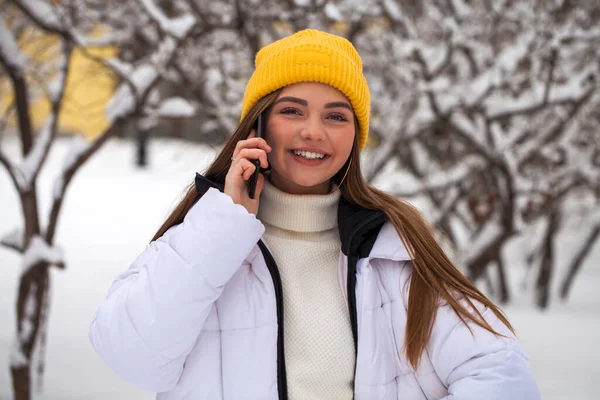 Jonge mooie vrouw met een mobiele telefoon in een winterpark — Stockfoto
