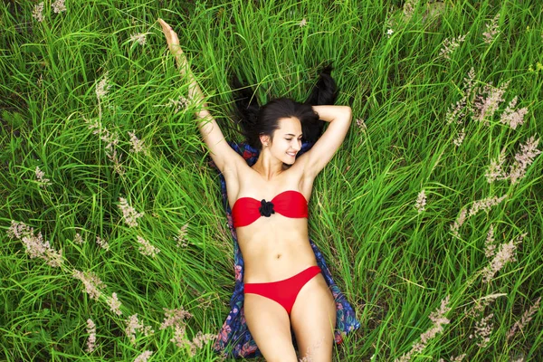 Mulher morena sexy em um maiô vermelho deitado no topo da grama — Fotografia de Stock