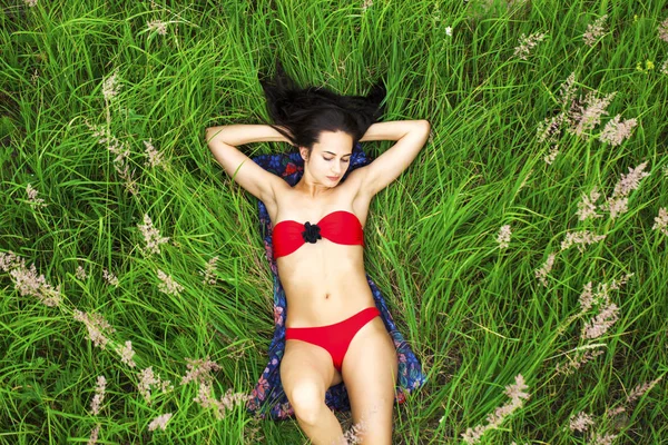 Sexy donna bruna in costume da bagno rosso sdraiato sulla cima dell'erba — Foto Stock