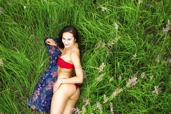 Sexy brunette woman in a red bathing suit lying on the grass top — Stock Photo, Image