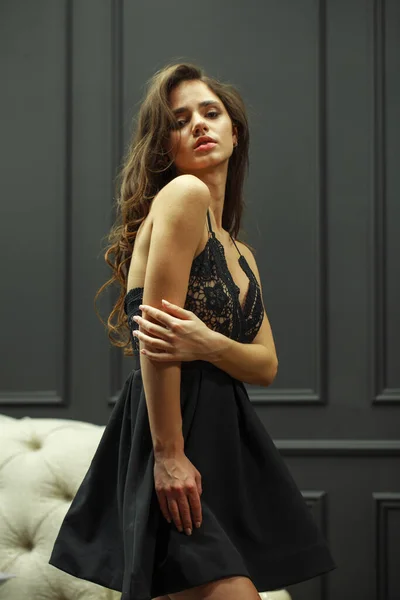 Morena jovem mulher em sexy vestido preto, estúdio parede interior — Fotografia de Stock