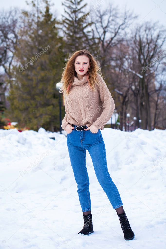 Portrait of a young beautiful blonde woman in beige sweater posing in winter park