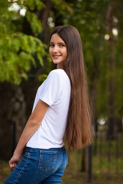 夏の公園の背景に白いTシャツの若い美しいブルネットの女の子の肖像画 — ストック写真