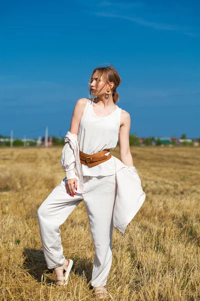 穿着米色西服的漂亮金发姑娘站在割破的田野里的干草堆后面 — 图库照片