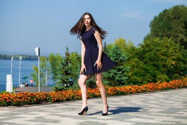 Mavi elbiseli, yaz caddesinde yürüyen neşeli bir kızın tam boy portresi.