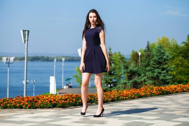 Mavi elbiseli, yaz caddesinde yürüyen neşeli bir kızın tam boy portresi.