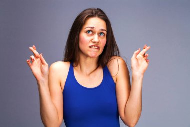 Beden dili ve duygular kavramı. Memnun koyu saçlı güzel memnun kız beggs Tanrı ona yardım için parmak çarpı işareti tutar, iyi şanslar diliyor, gri studio arka plan üzerinde kapalı izole dua ediyor.