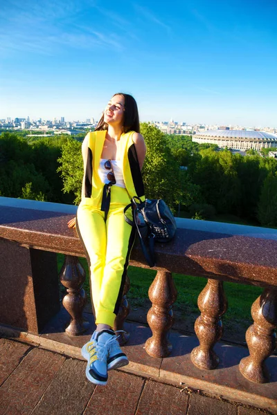 在莫斯科麻雀山的背景下 身穿黄色连衣裙的漂亮女人坐在栏杆上 — 图库照片