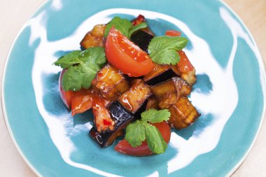 Mavi tabakta soslu kızarmış patlıcan ve domates salatası