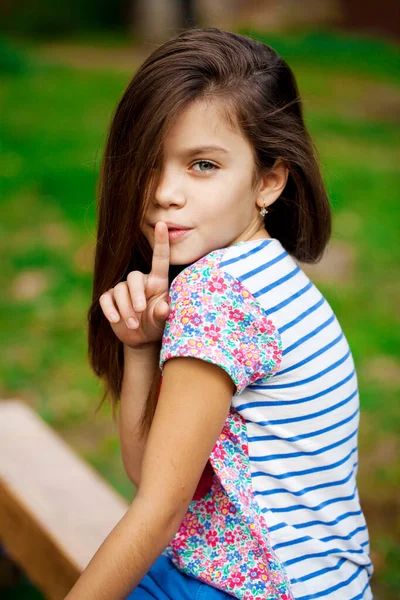 年轻漂亮的小女孩已经把食指放在嘴唇上作为标志的沉默 在户外夏天 — 图库照片