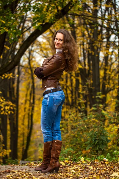 秋天公园里一个穿着蓝色牛仔裤的年轻漂亮姑娘的全身像 — 图库照片