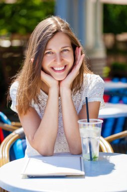 Sokakta bir kafede oturan soğuk bir içecekle güzel esmer bir kadın.