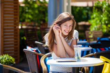 Sokakta bir kafede oturan soğuk bir içecekle güzel esmer bir kadın.