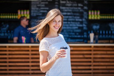 Kahvenin arka planında kağıt bardakla genç ve güzel bir kadın. Yazın açık havada.