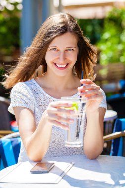 Sokakta bir kafede oturan soğuk bir içecekle güzel esmer bir kadın.