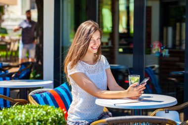 Sokakta bir kafede oturan soğuk bir içecekle güzel esmer bir kadın.