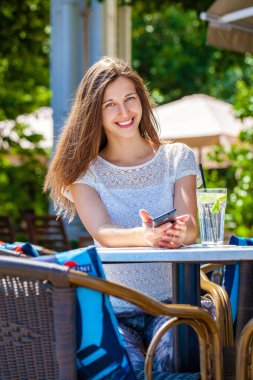 Sokakta bir kafede oturan soğuk bir içecekle güzel esmer bir kadın.