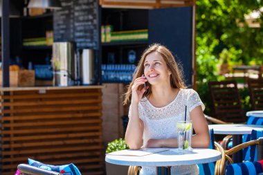 Açık hava kafesinde telefonla arayan mutlu esmer kadın.