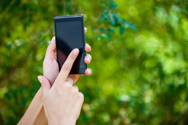 Side view of a woman\'s hand holding a modern slick smartphone while dialing with her thumb against summer green background