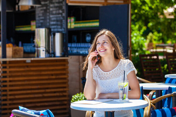 Happy brunette woman calling by phone in open air cafe