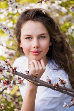 Güzel genç kız çiçek açan kiraz ağacının yanında beyaz çiçeklerle poz veriyor. Bahar geldi. 