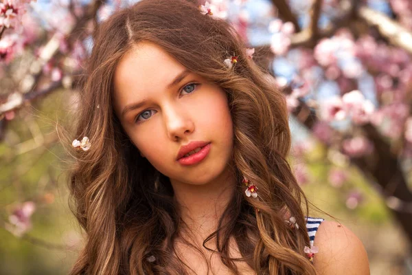 ピンクの花を持つ桜の木の近くにポーズ美少女10代 春の公園 — ストック写真