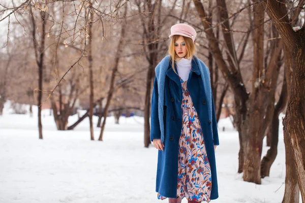 化妆的美 一个身穿蓝色外套 头戴粉色帽子的金发姑娘在冬季公园摆姿势的画像 — 图库照片