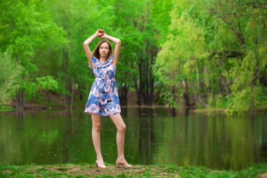 Göl kenarında poz veren mavi elbiseli güzel bir kadının vücut portresi.