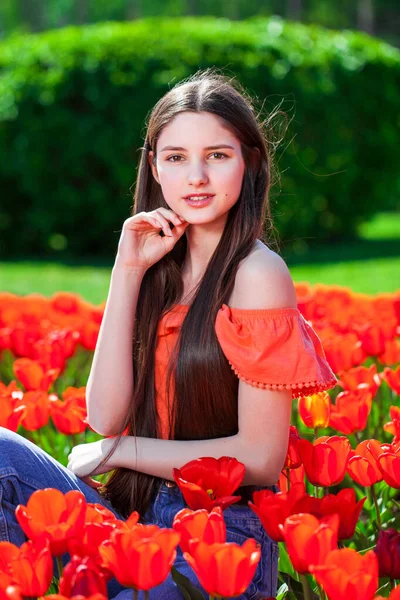 一个年轻美丽的女孩在红色郁金香的背景下摆姿势的画像 — 图库照片