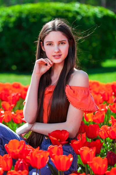 一个年轻美丽的女孩在红色郁金香的背景下摆姿势的画像 — 图库照片