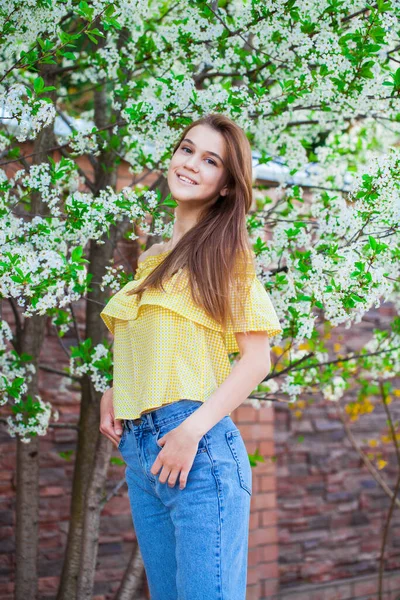 満開の桜を背景に 黄色のブラウスに若いスタイリッシュな女の子の肖像画を閉じます — ストック写真