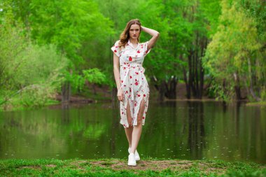 Göl kenarında poz veren beyaz elbiseli güzel bir kadının vücut portresi.